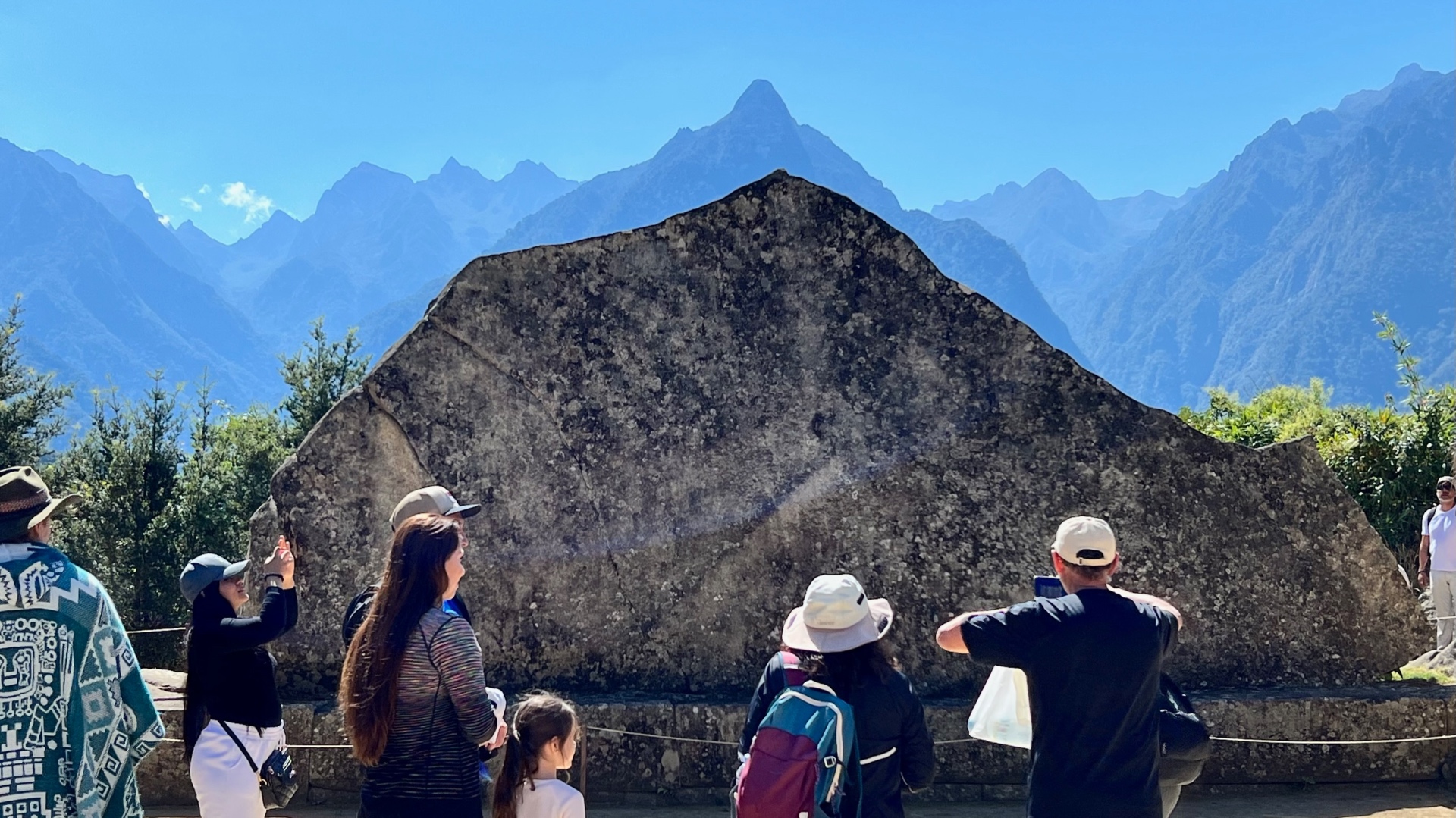 Visitors gathered around a monumental sacred stone with distant peaks beyond