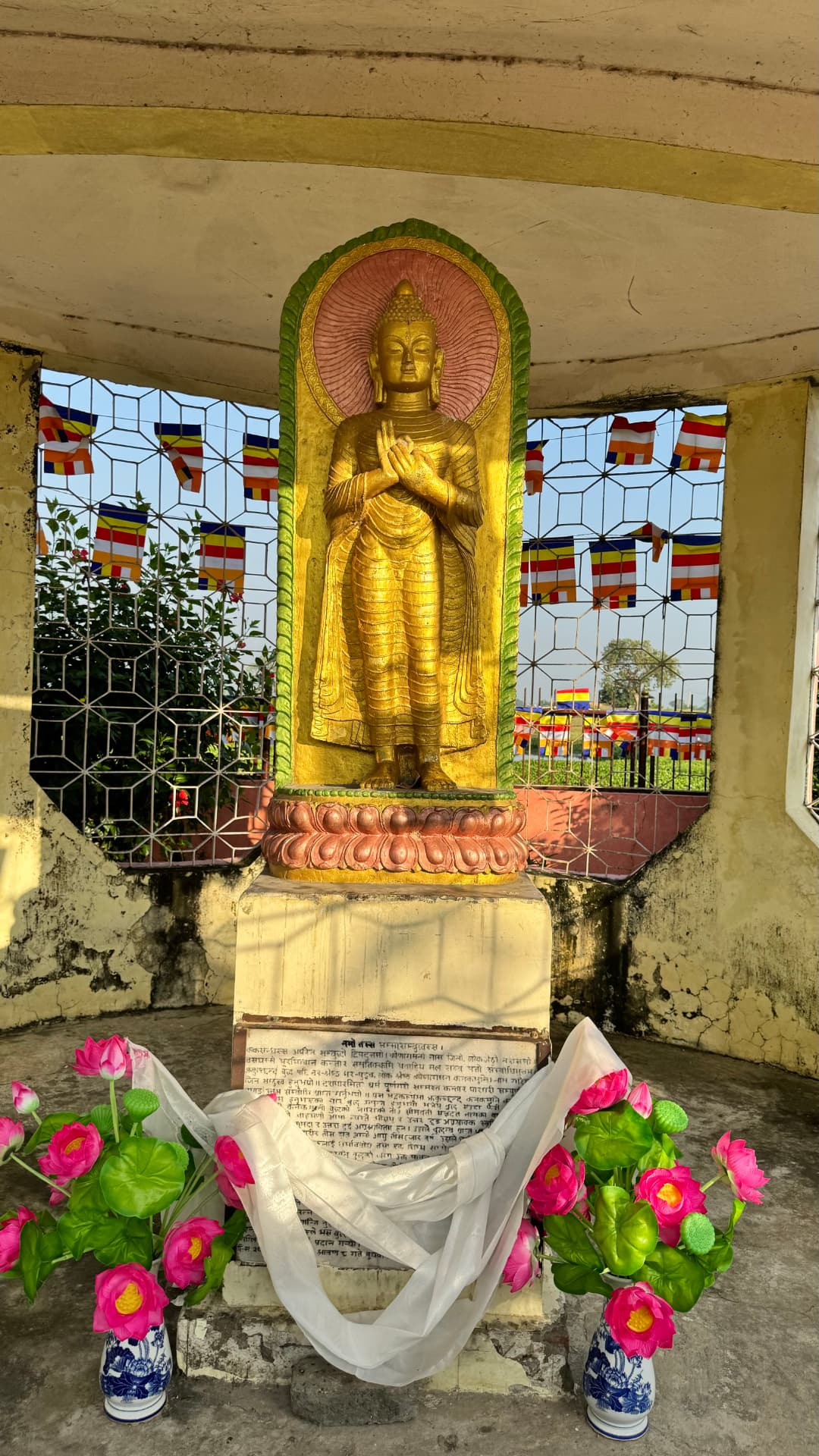 A golden standing Buddha surrounded by flowers and Buddhist flags. — Lumbini, Nepal.