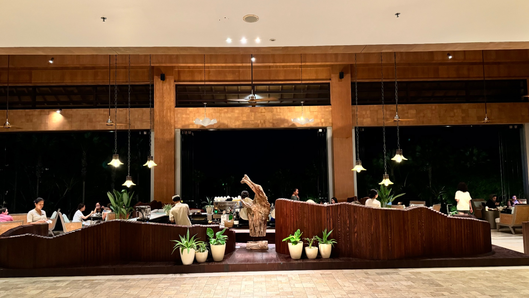 Warmly lit open-air lounge with hanging lights and curved timber counters