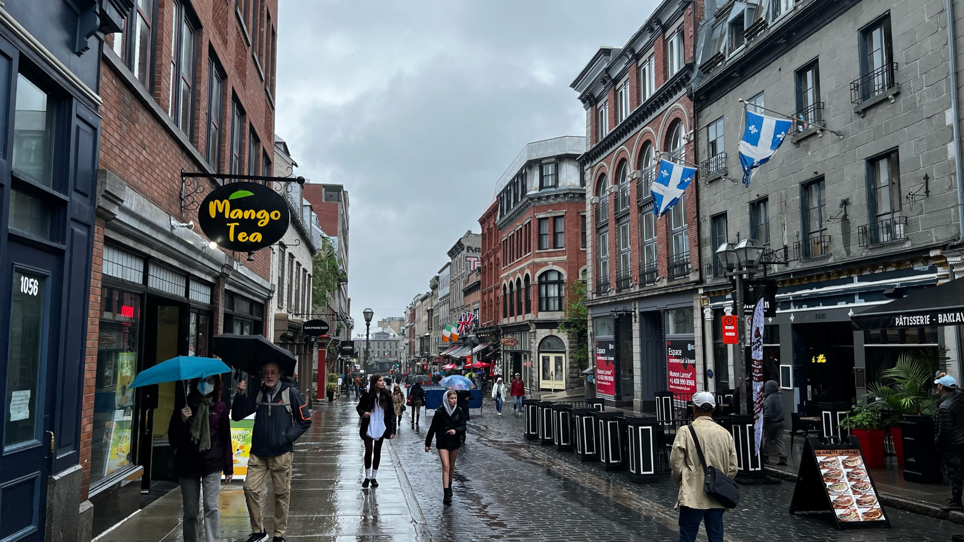 Rainy pedestrian street lined with historic buildings and Québec flags