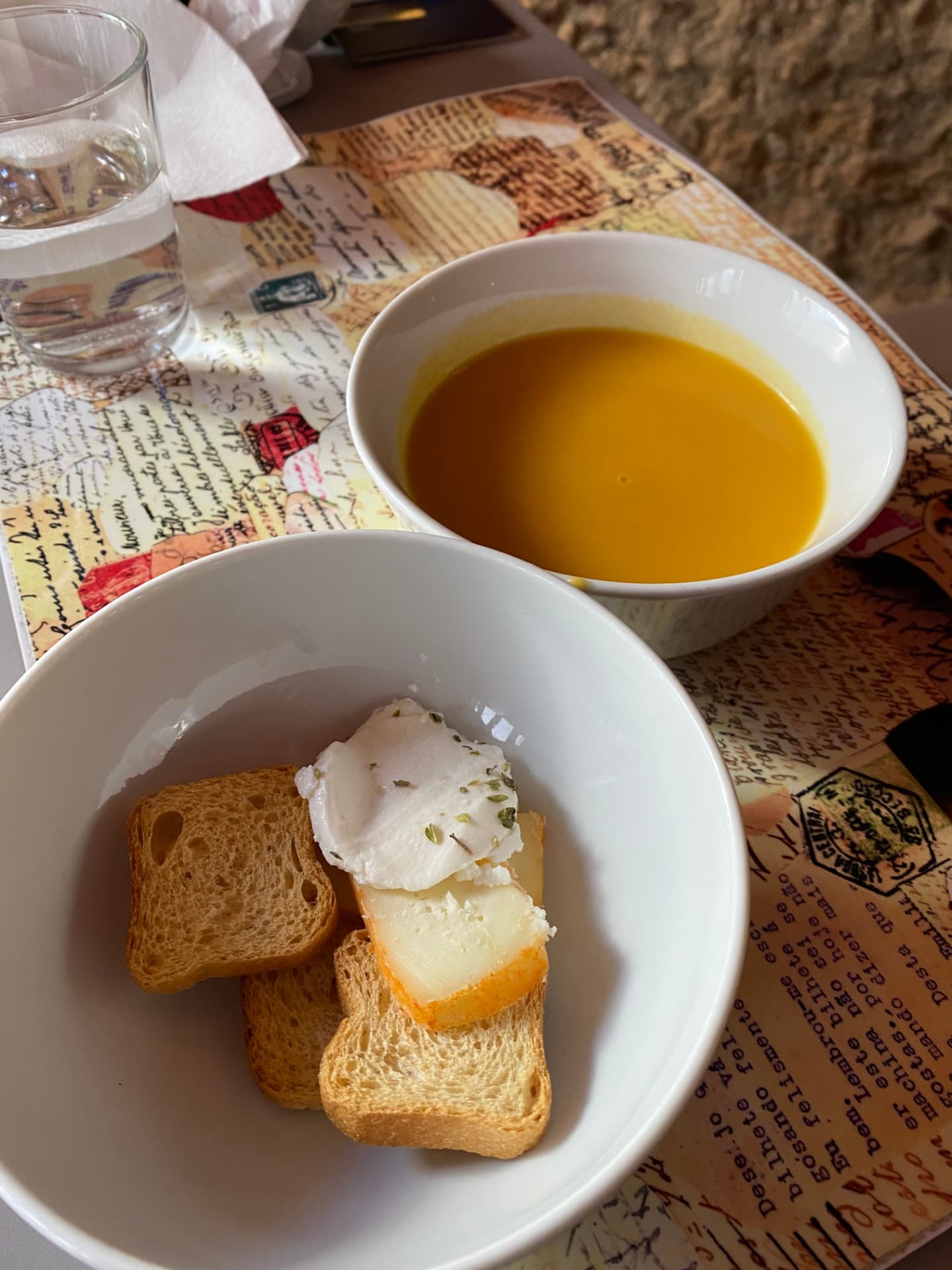 A bowl of orange soup beside a bowl of bread