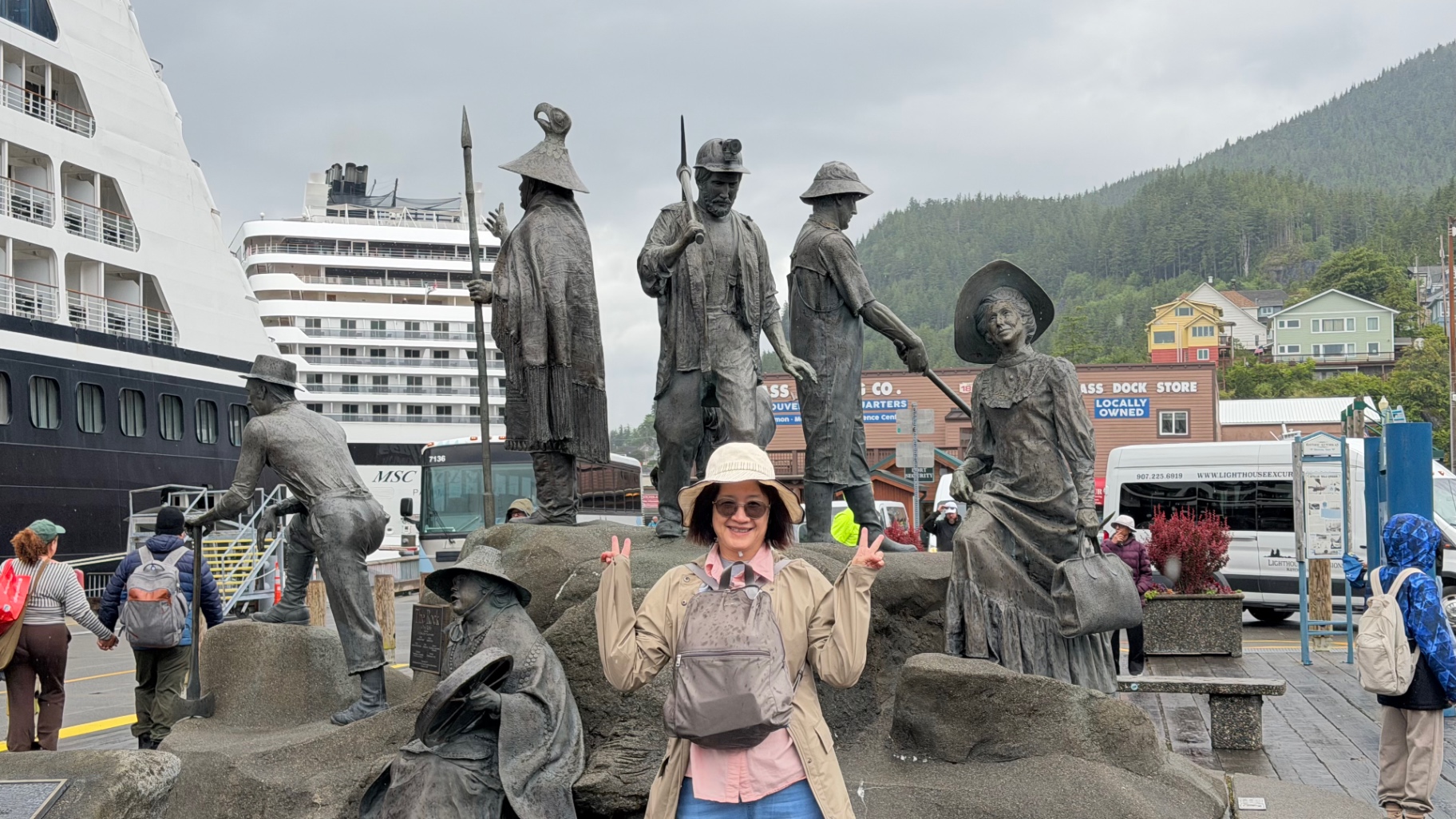 Becky standing in front of Ketchikan's bronze Rock pioneers sculpture group, making peace signs and smiling