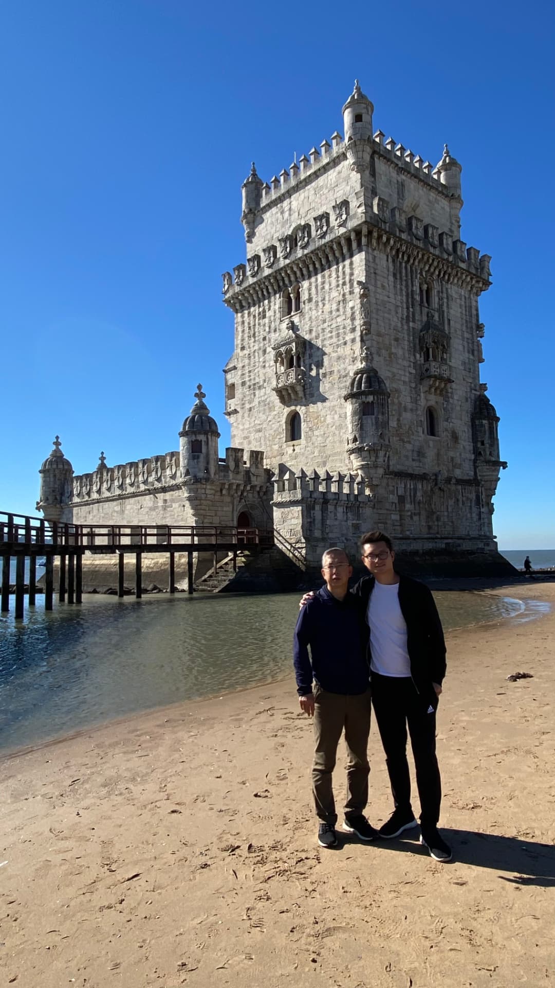 Two companions standing on the sand with Belém Tower behind
