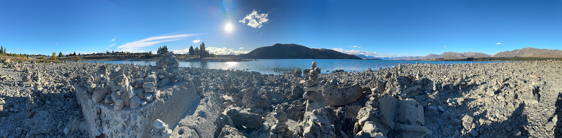 A panoramic view of the cairn-covered shore, the blue lake, and surrounding mountains under a clear sky