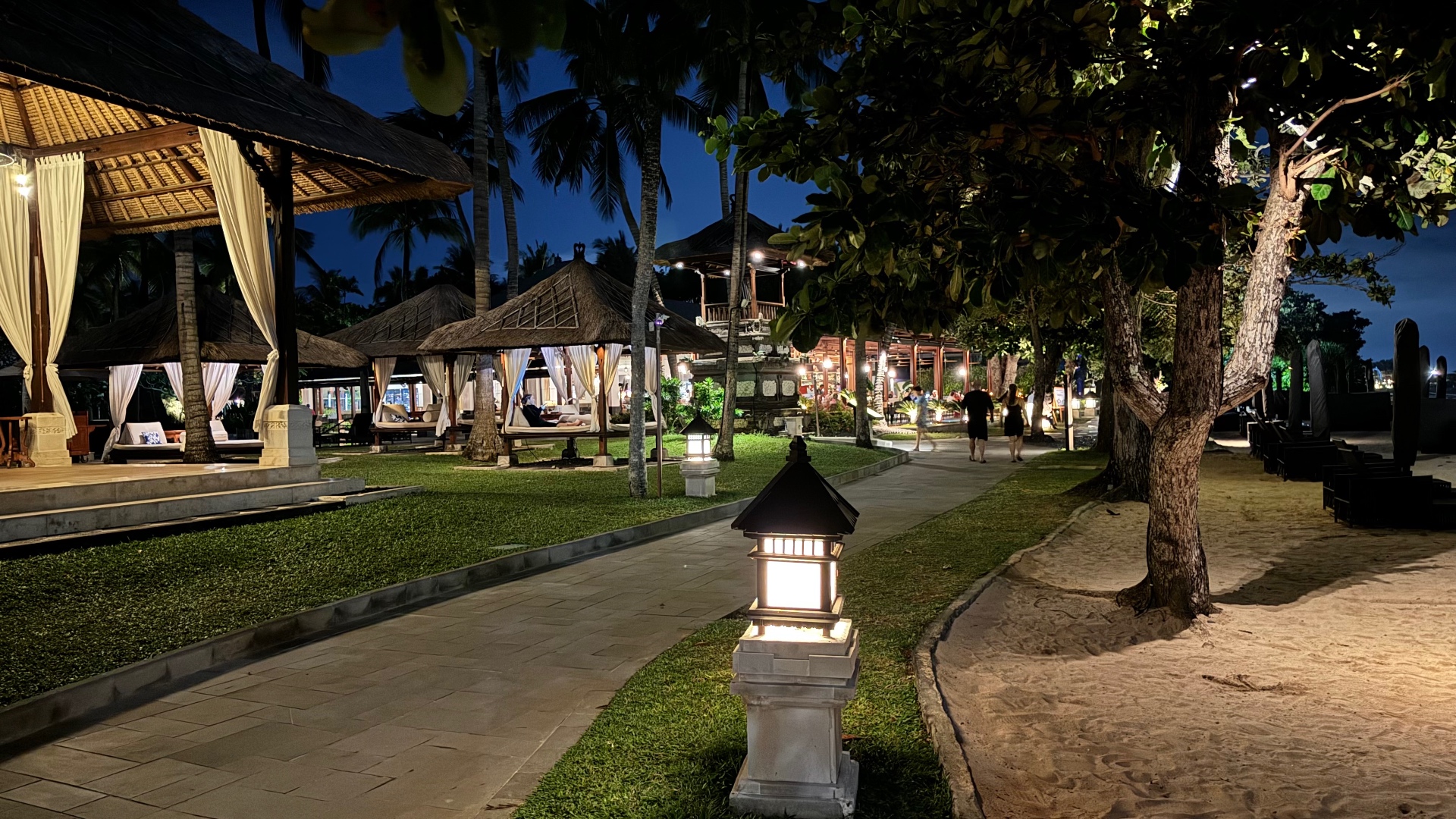 Lantern-lit path between beach cabanas and the sand at night