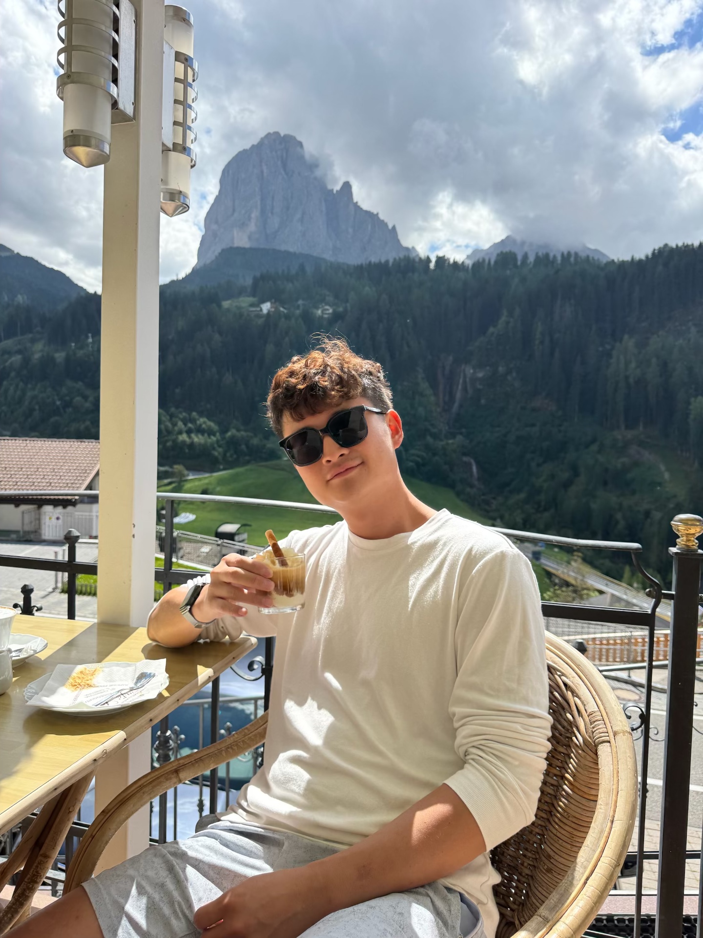 Kayden enjoying a drink on a sunny terrace with a Dolomites peak behind him