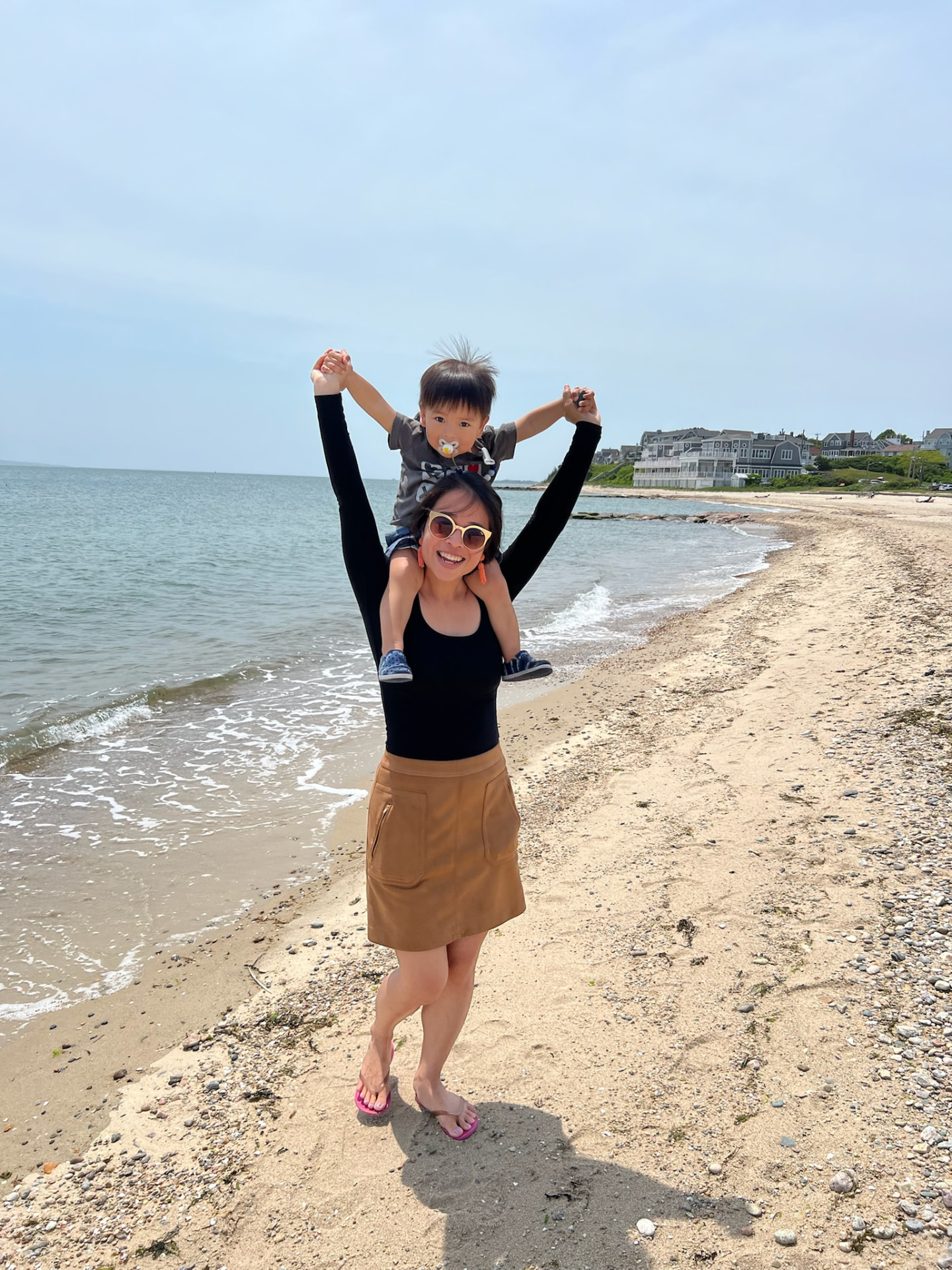 A mother carrying her young son on her shoulders along a New England beach