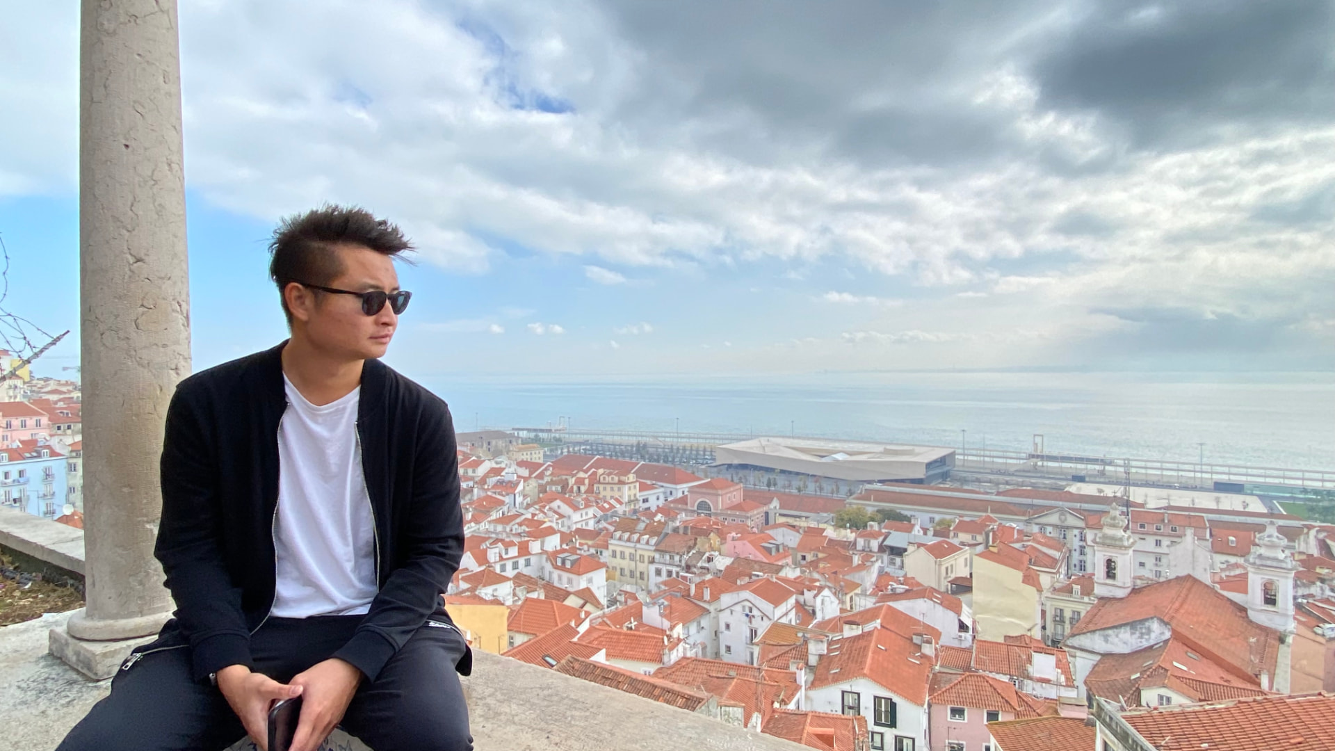 A man sitting on a stone wall above Lisbon's red-tiled roofs