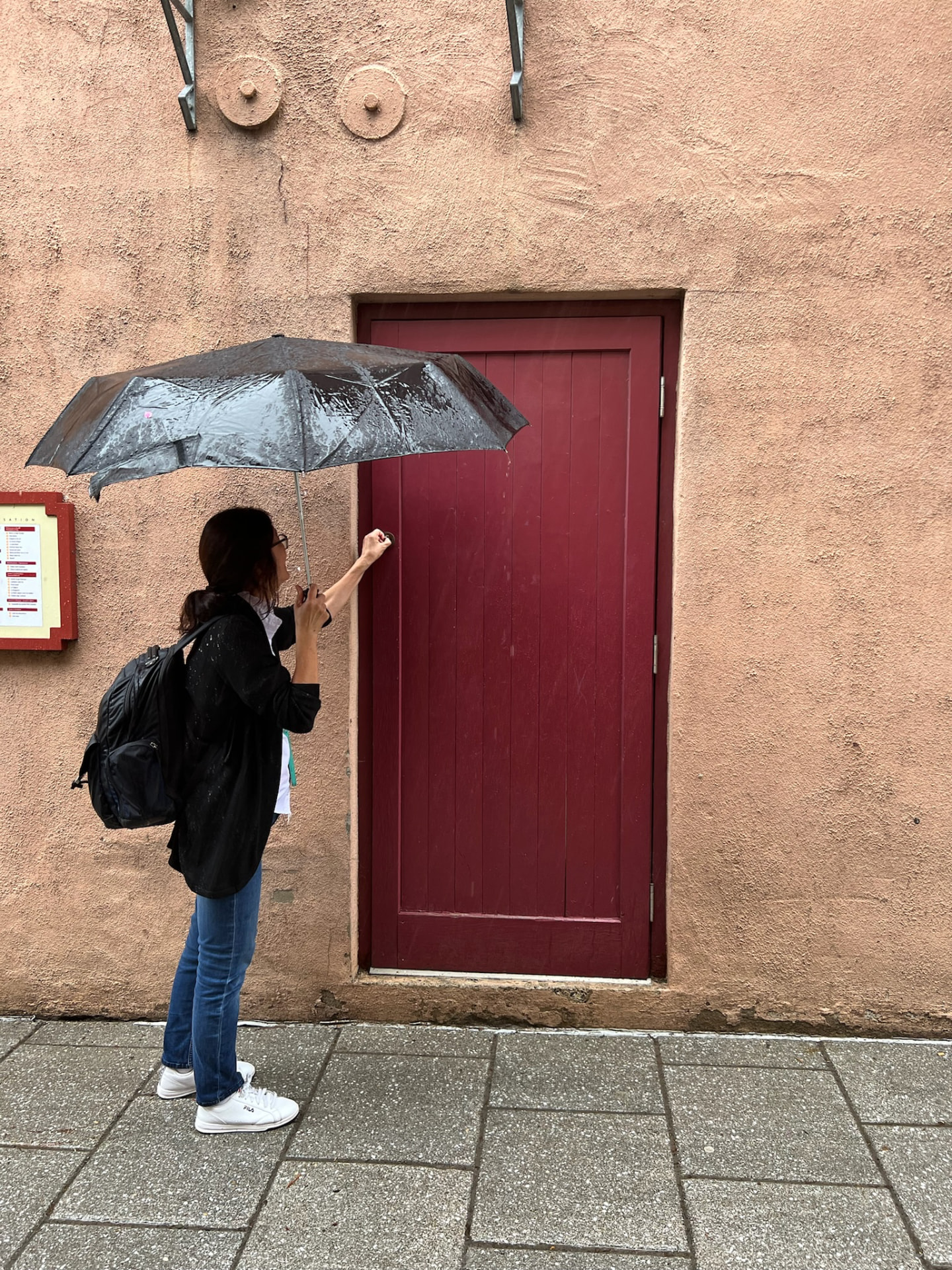 Woman with an umbrella knocking on the red Goblin door in Petit Champlain