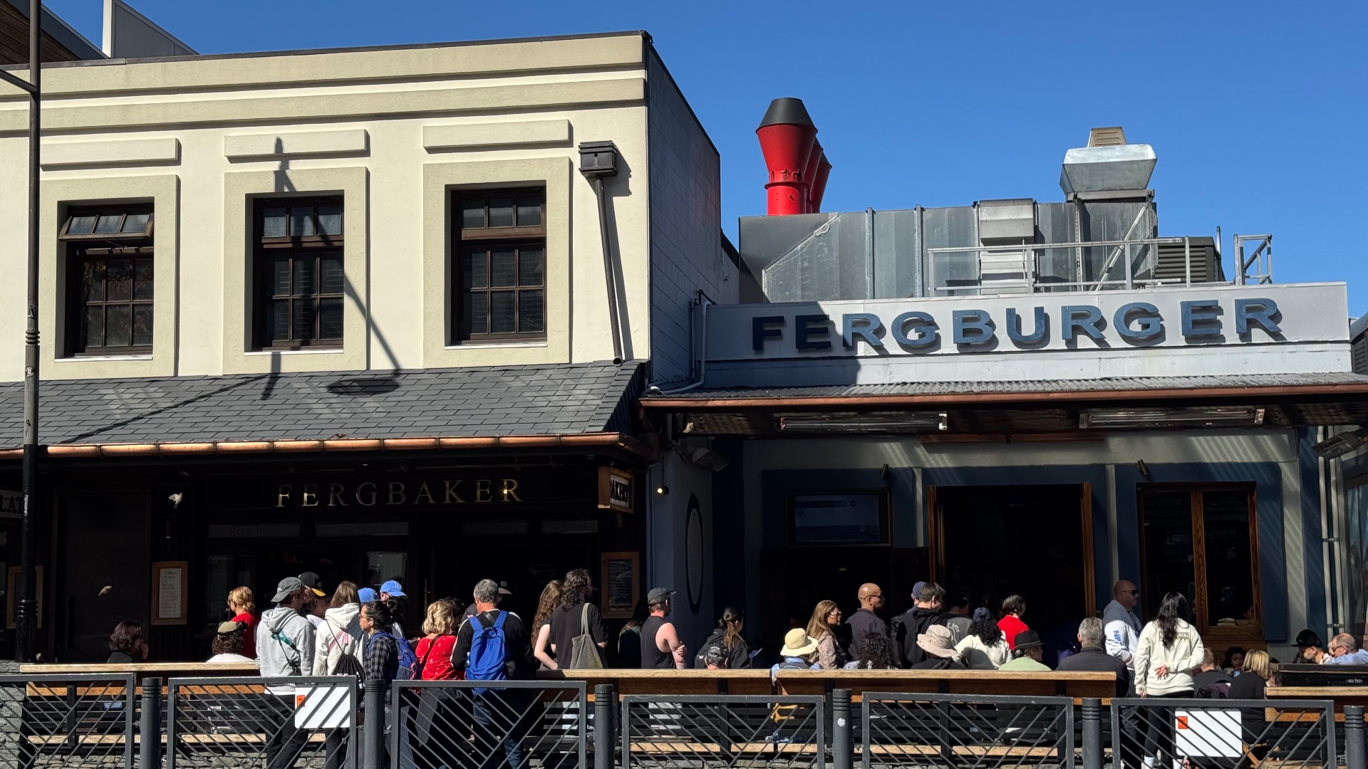 The Fergburger storefront in Queenstown in bright daylight, with a long queue of customers waiting outside