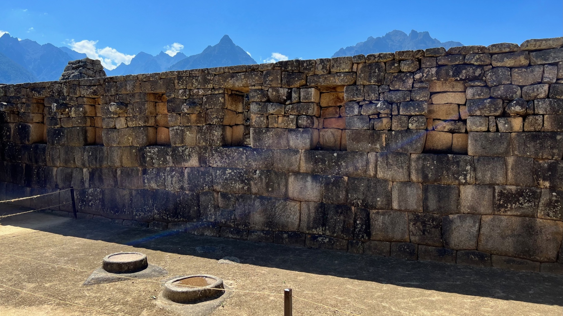 Long stone wall with recessed windows and mountain peaks visible above it