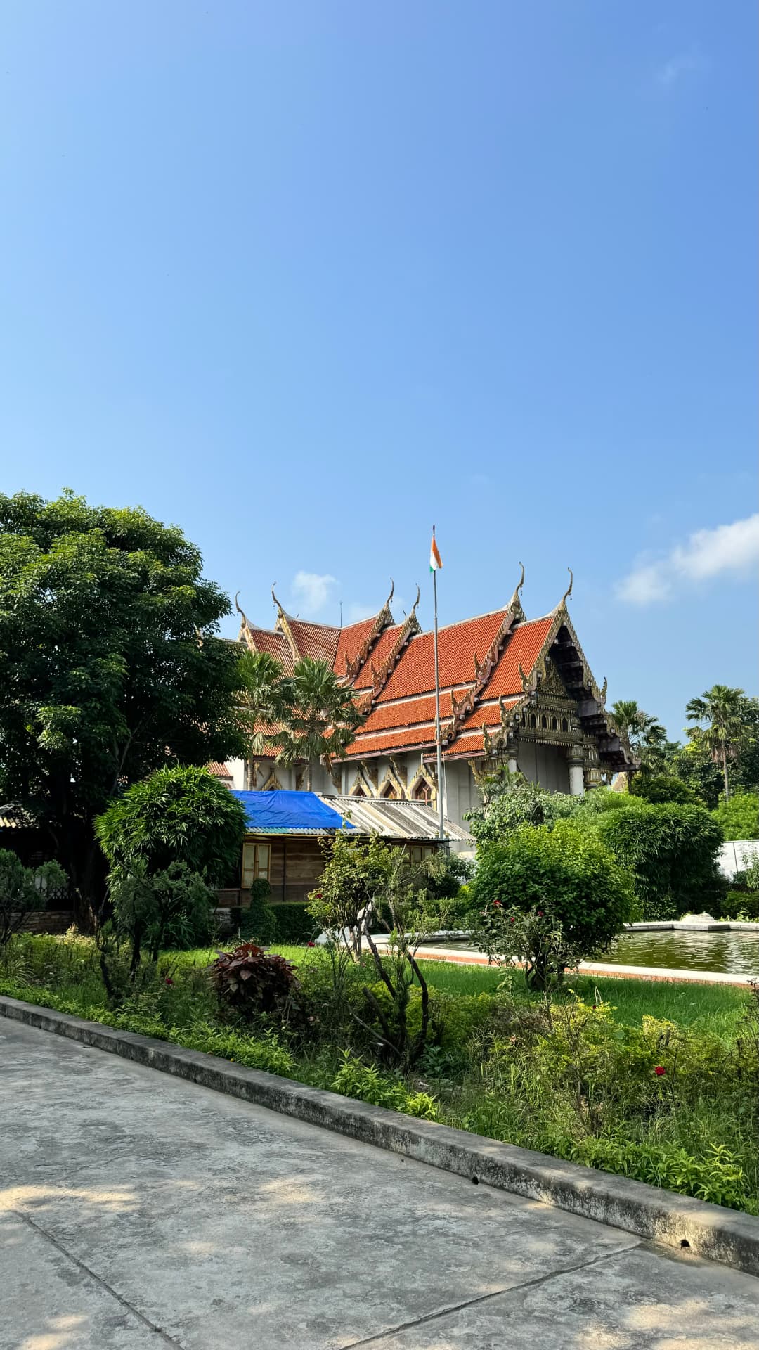 The Thai-style temple roof appears above a green garden. — Bodh Gaya, Bihar, India.