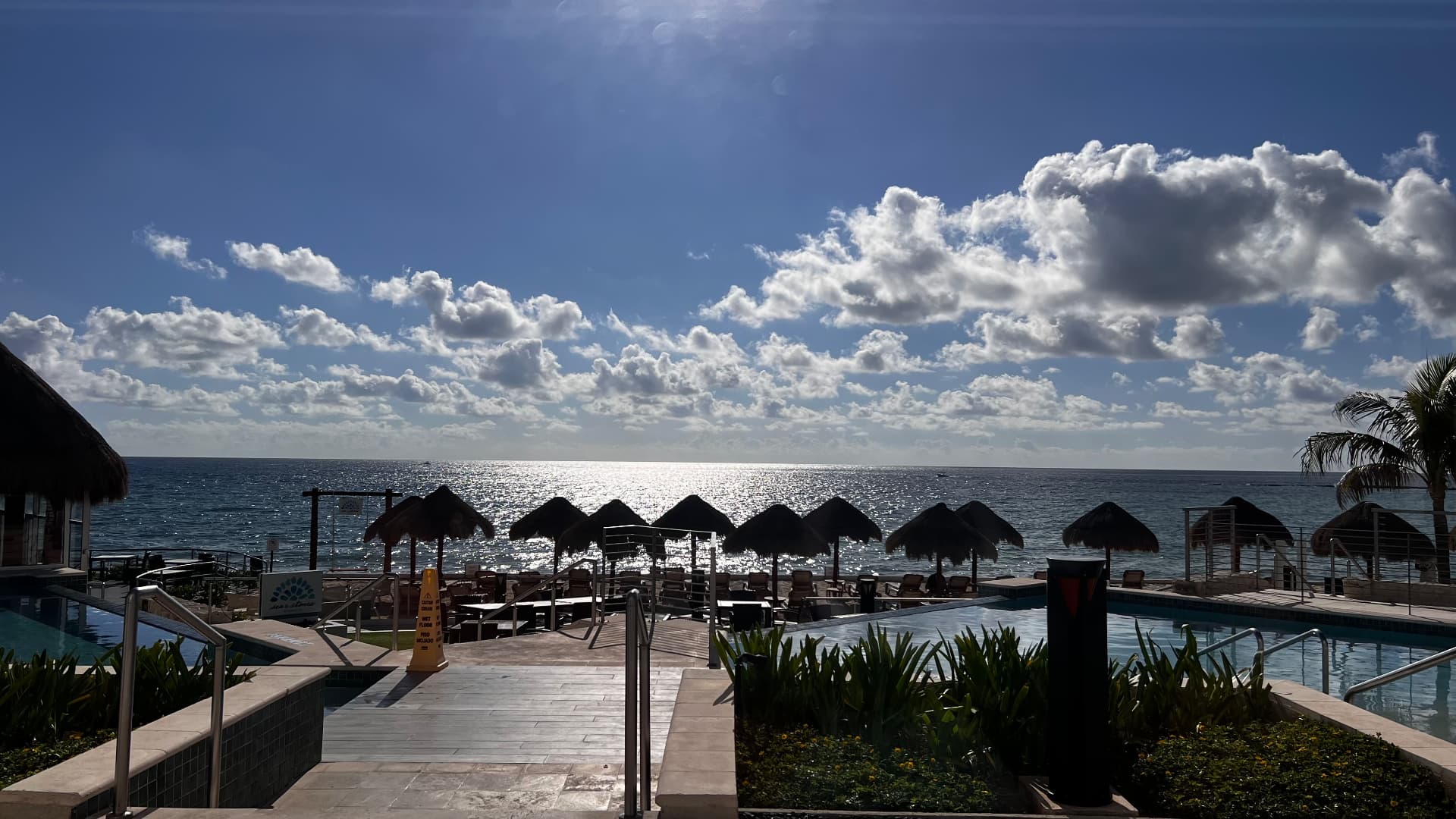 Sunlight sparkling beyond pools and a row of palapas