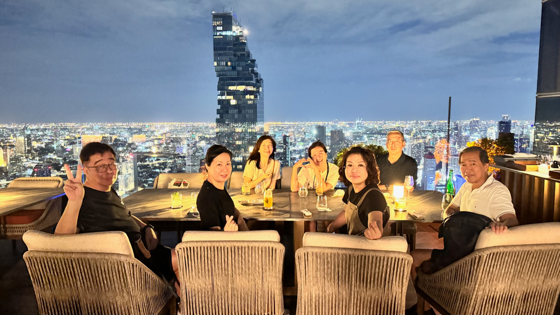 Friends posing at a rooftop table over Bangkok