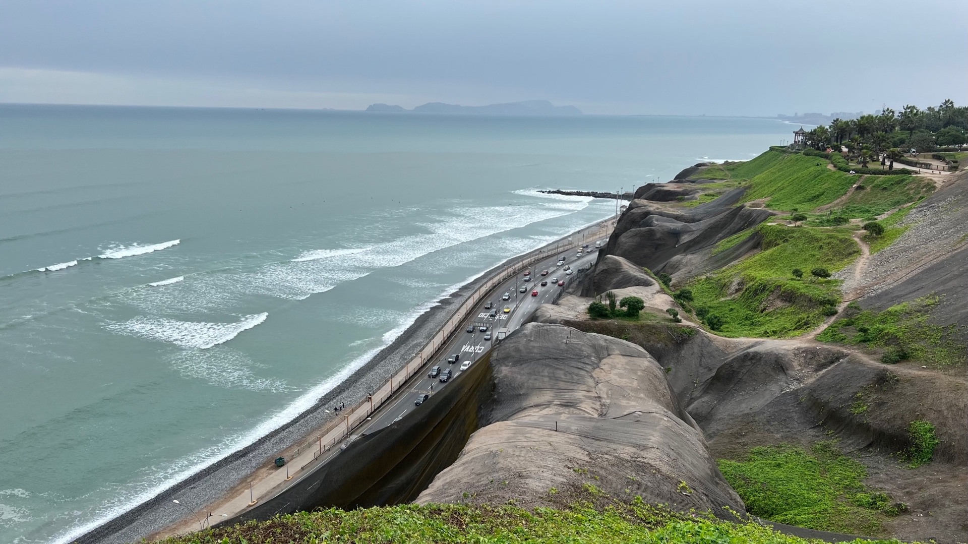 Pacific waves rolling below the green clifftops and coastal road of Lima