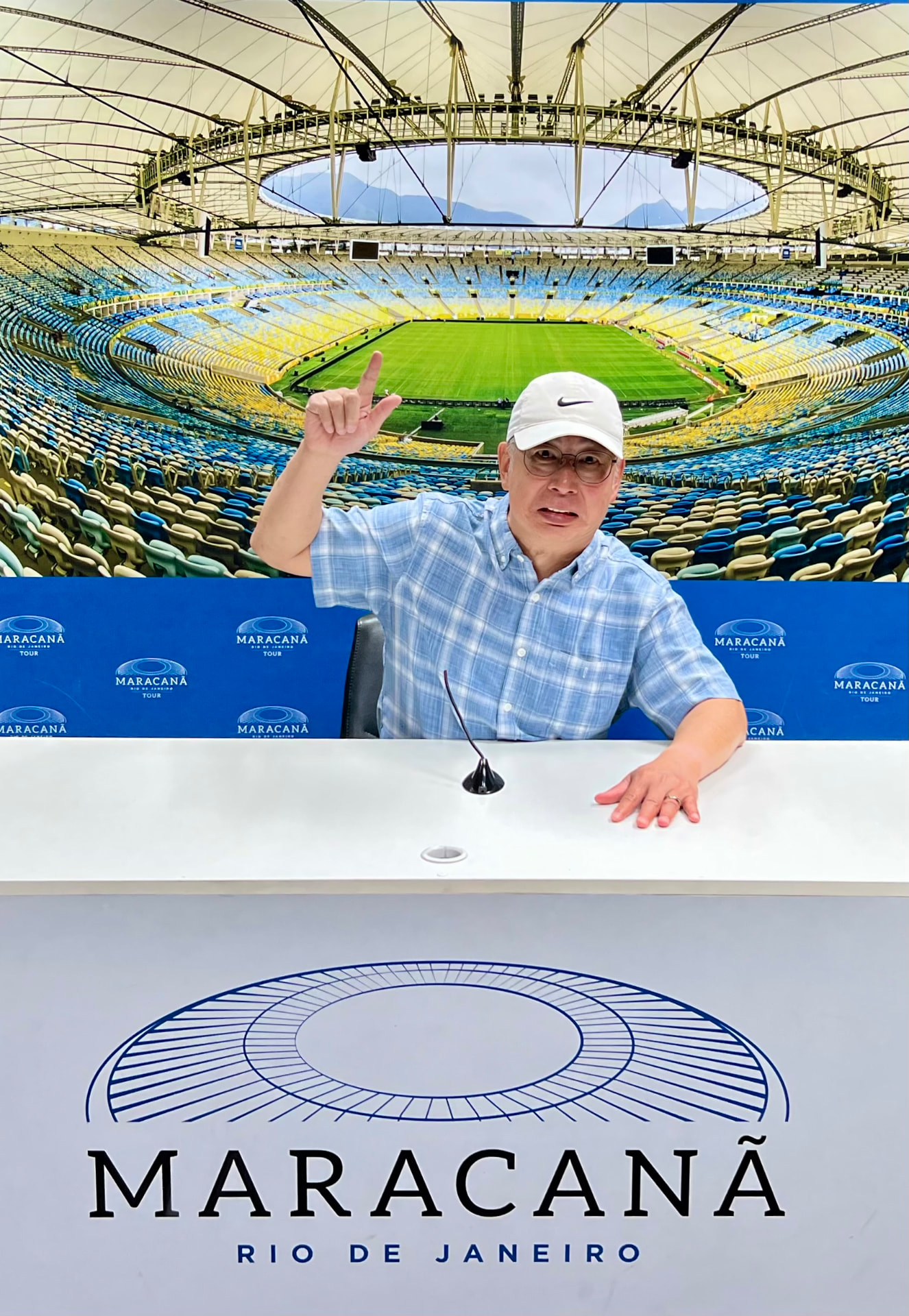 Ken seated at a Maracanã tour press desk with the stadium behind him