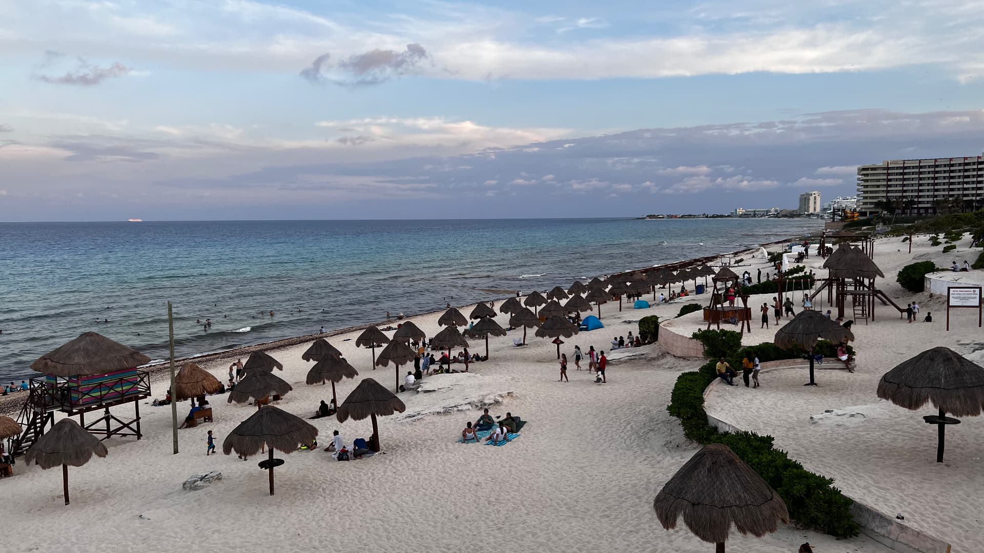 Beachgoers beneath palapa umbrellas beside the Caribbean