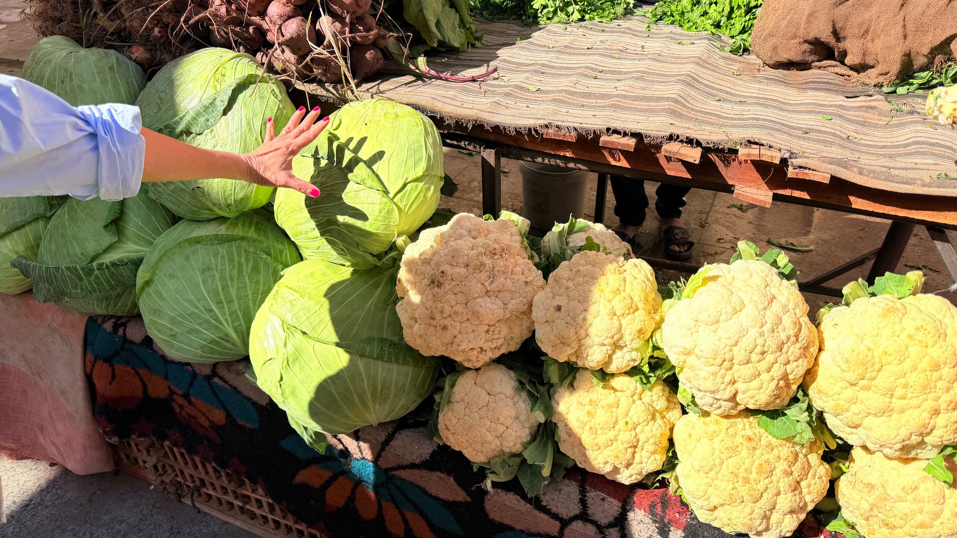 Cabbages and cauliflowers stacked on a patterned rug at a market stall