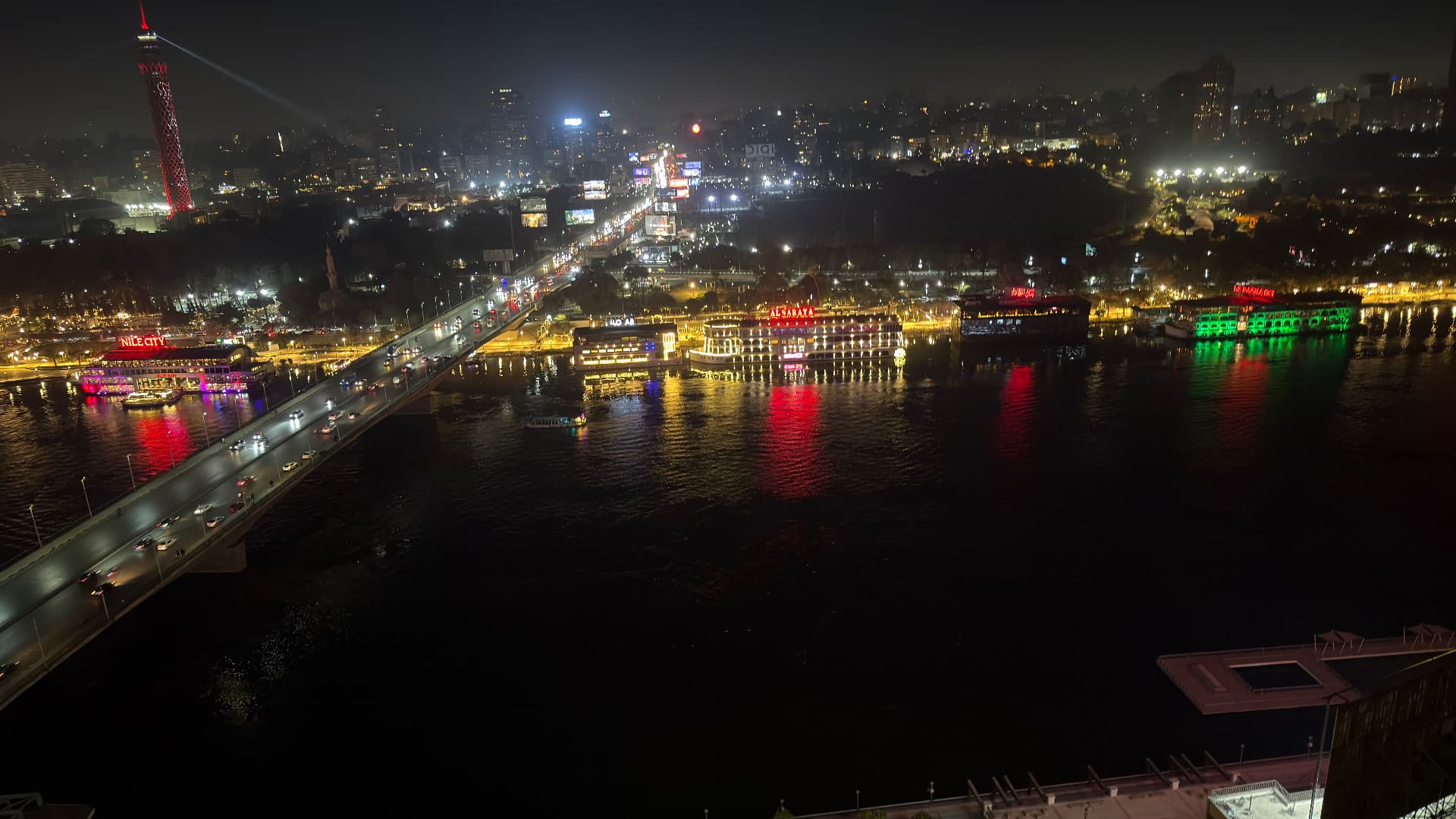 The Nile in Cairo at night, a lit bridge crossing the water with floating restaurants and the Cairo Tower glowing red