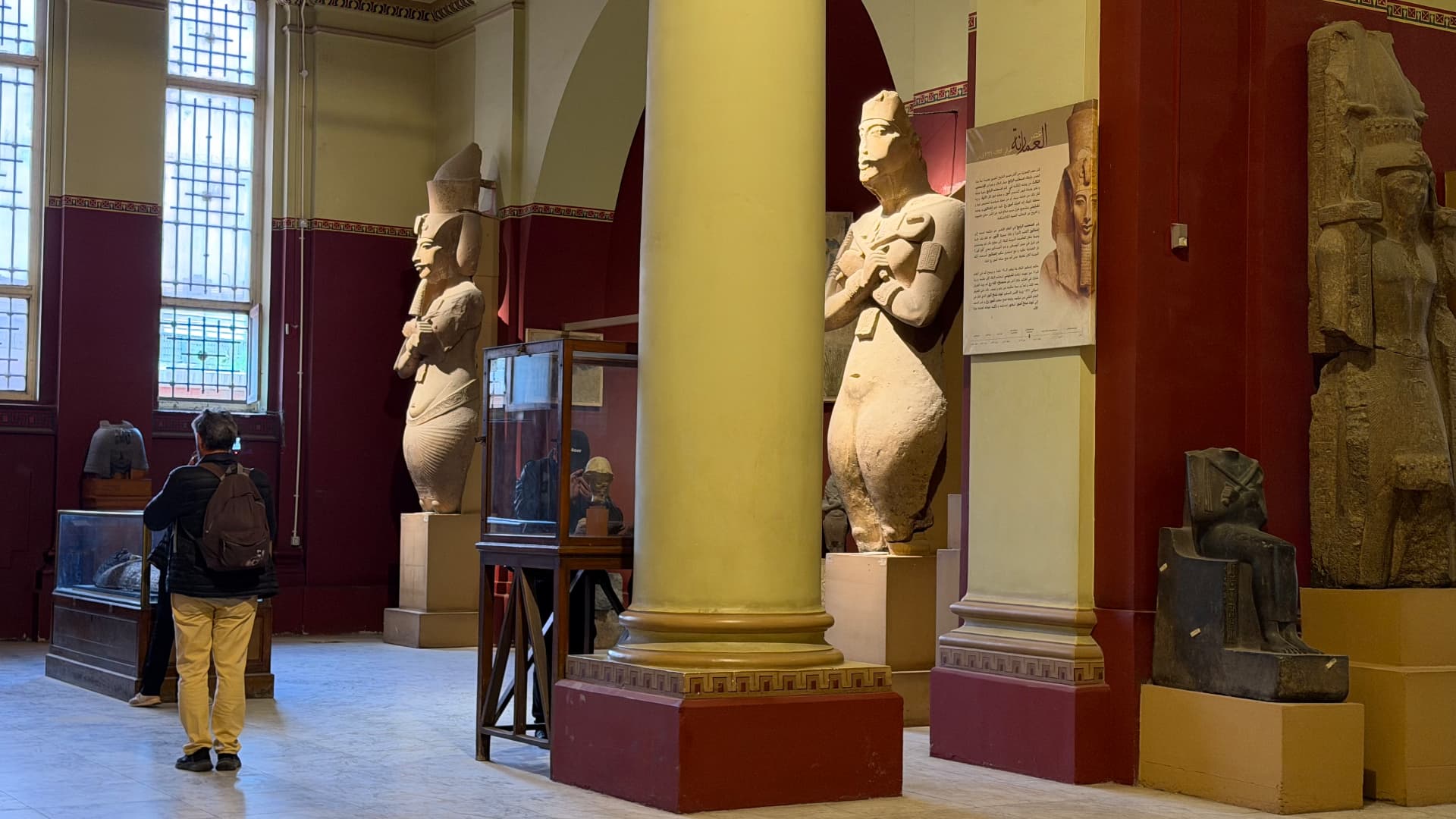 A museum gallery with colossal standing statues of Akhenaten beside painted columns
