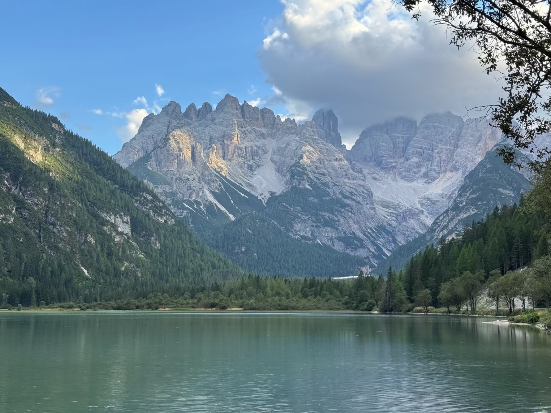 A calm alpine lake reflecting a vast crown of pale Dolomites peaks