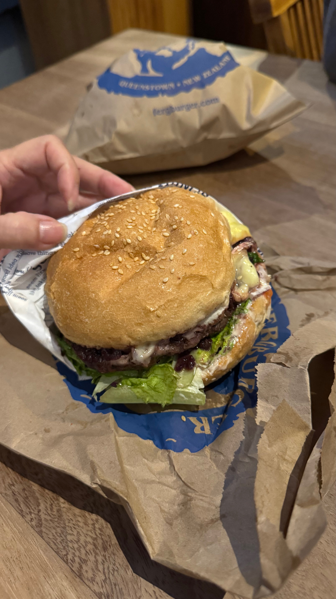 A close-up of a beef burger with lettuce and cheese, held in branded Fergburger wrapping