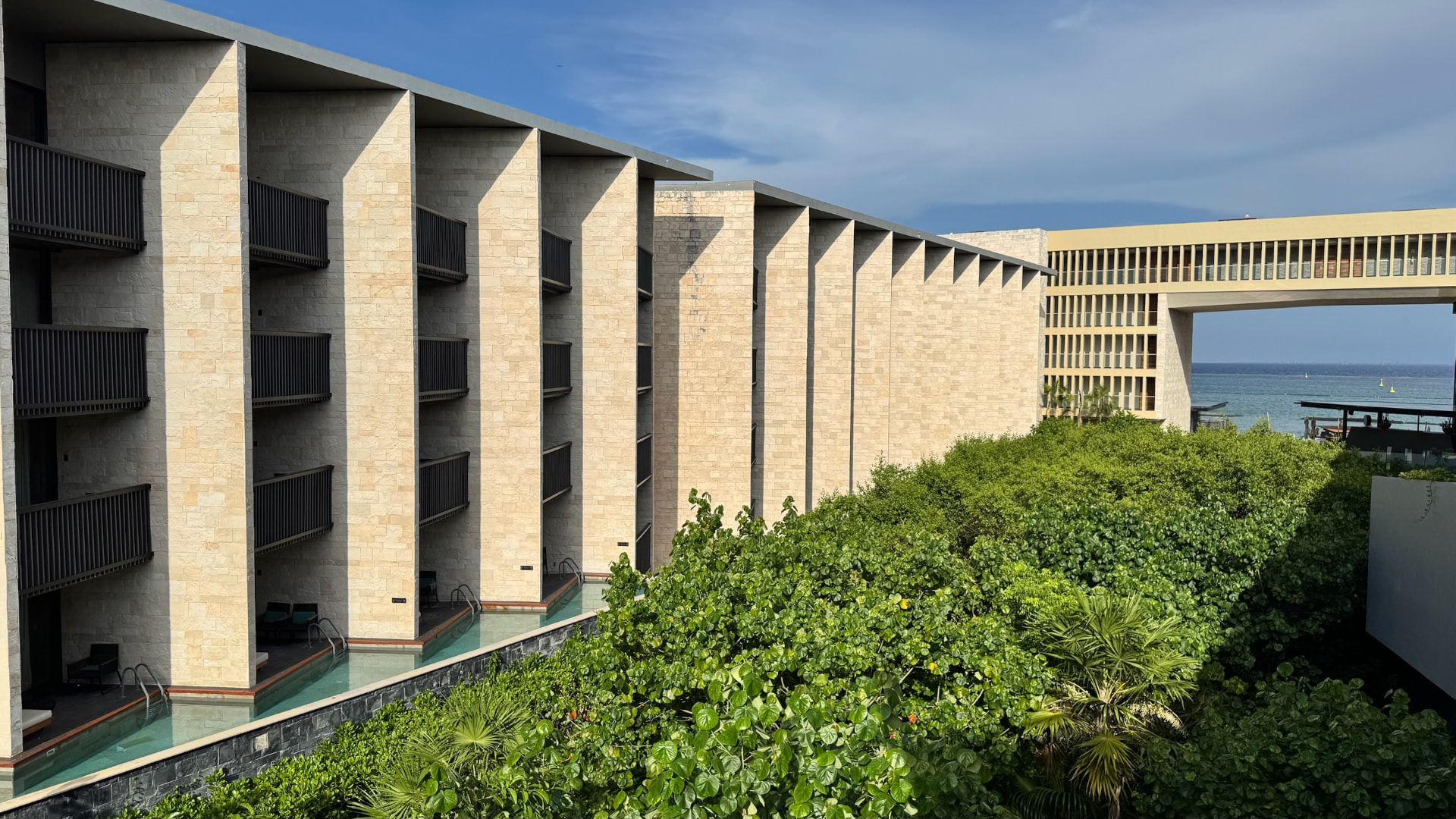 Modern stone hotel wings framing dense tropical planting and the sea