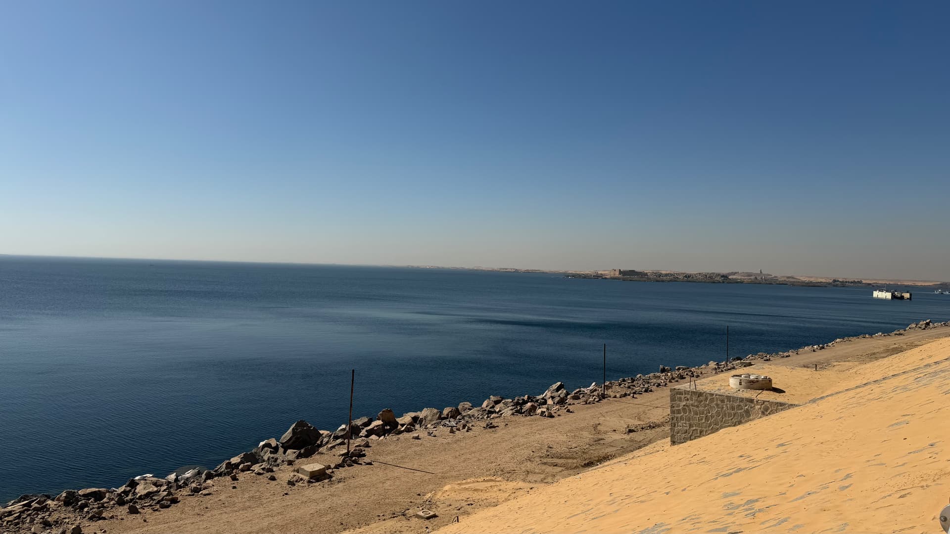 Lake Nasser stretching to the horizon behind the Aswan High Dam, with a sandy embankment in the foreground