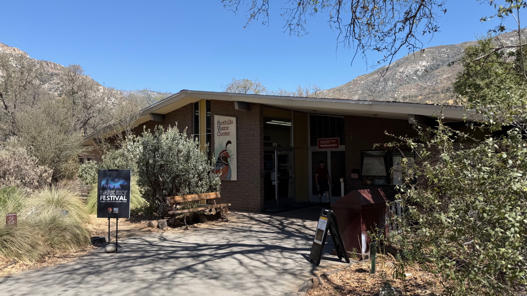 Foothills Visitor Center building below dry Sierra Nevada hills under a clear blue sky