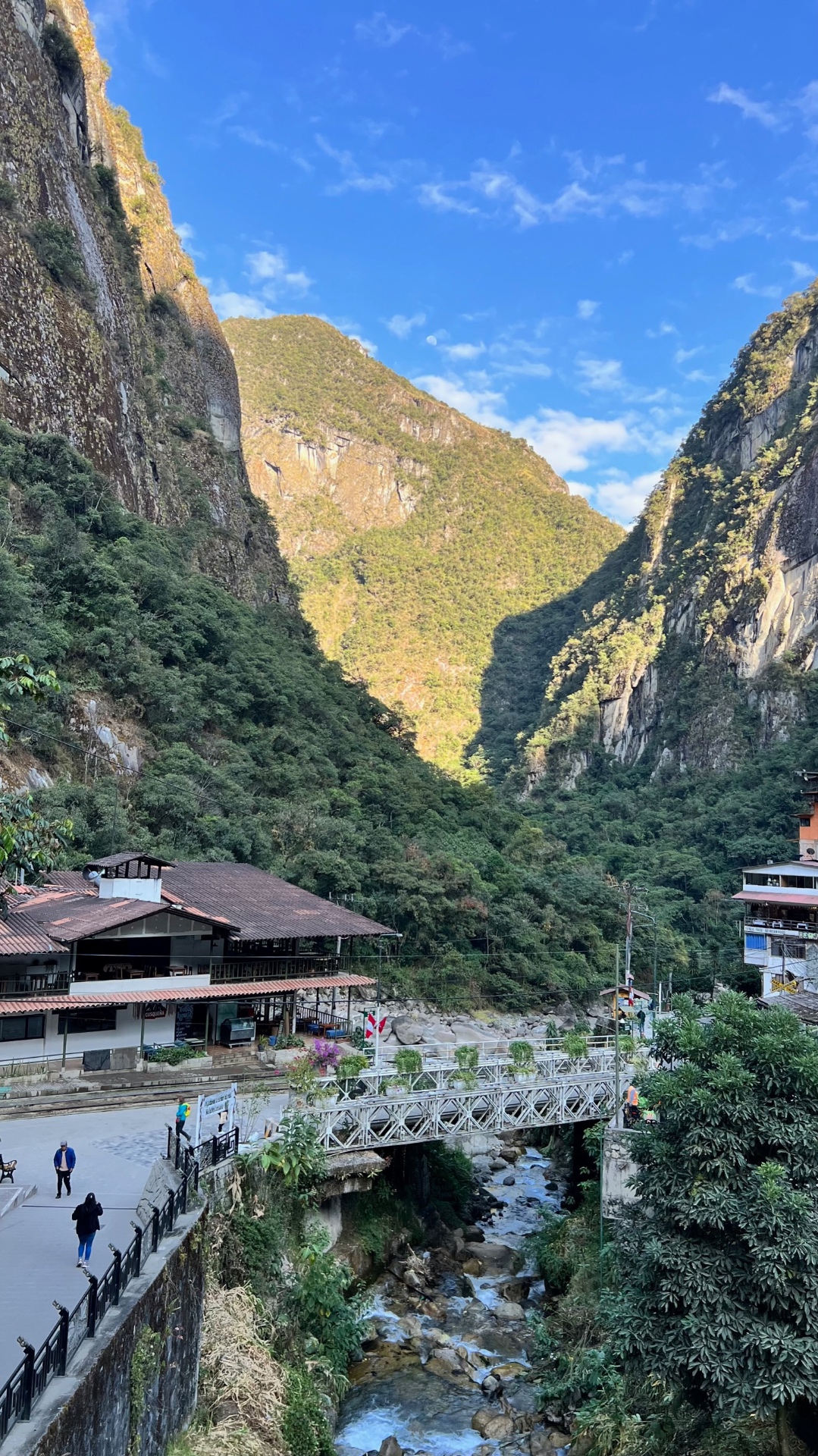 Aguas Calientes footbridge and stream framed by steep green mountain walls
