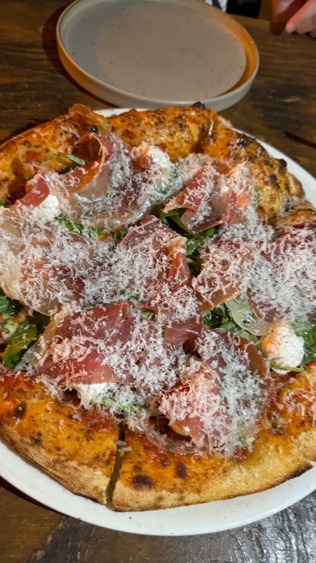 Wood-fired pizza topped with prosciutto, greens, and grated cheese
