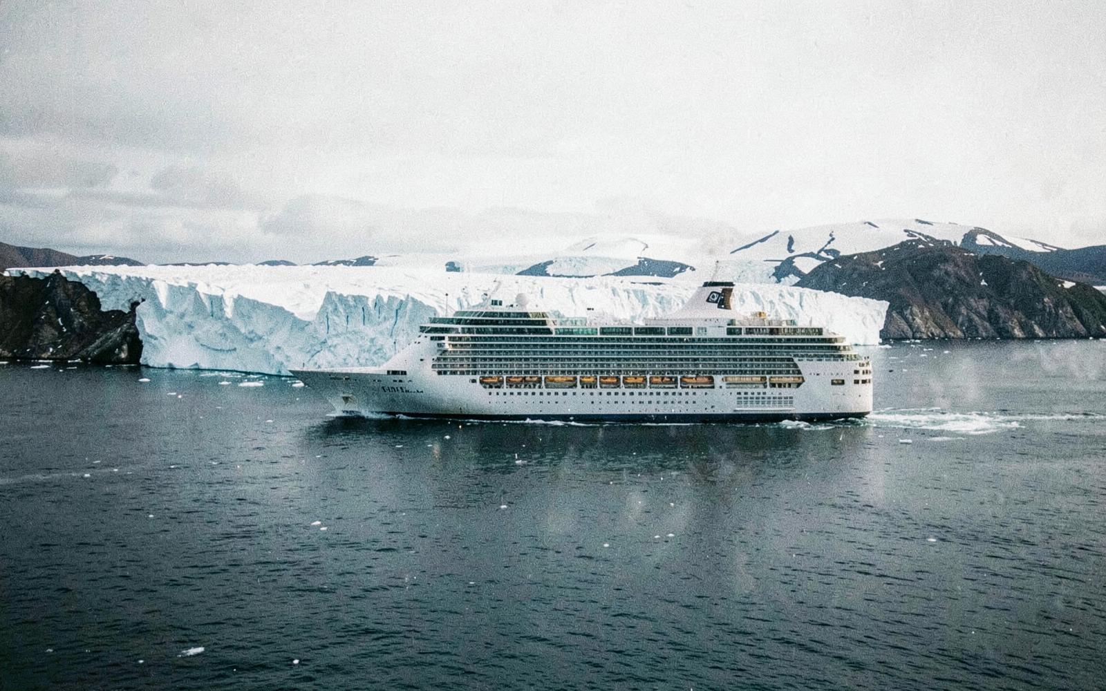 A cruise ship passing a tidewater glacier under a pale Alaskan sky