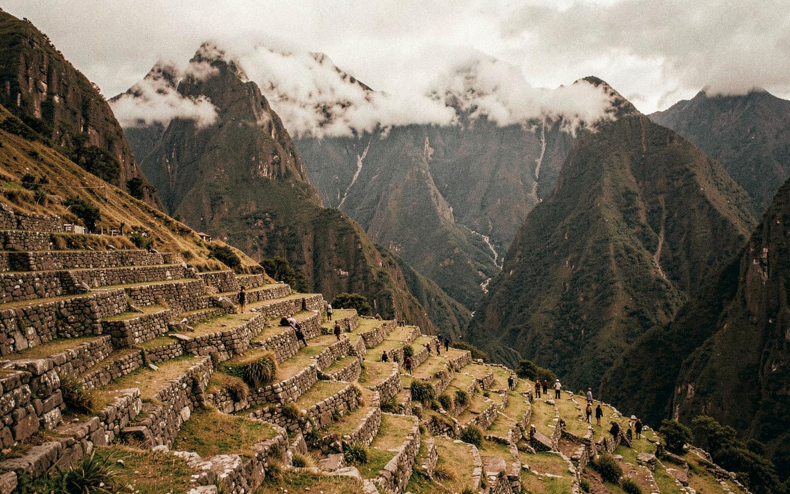 Ancient Andean stone terraces with cloud-wrapped peaks behind