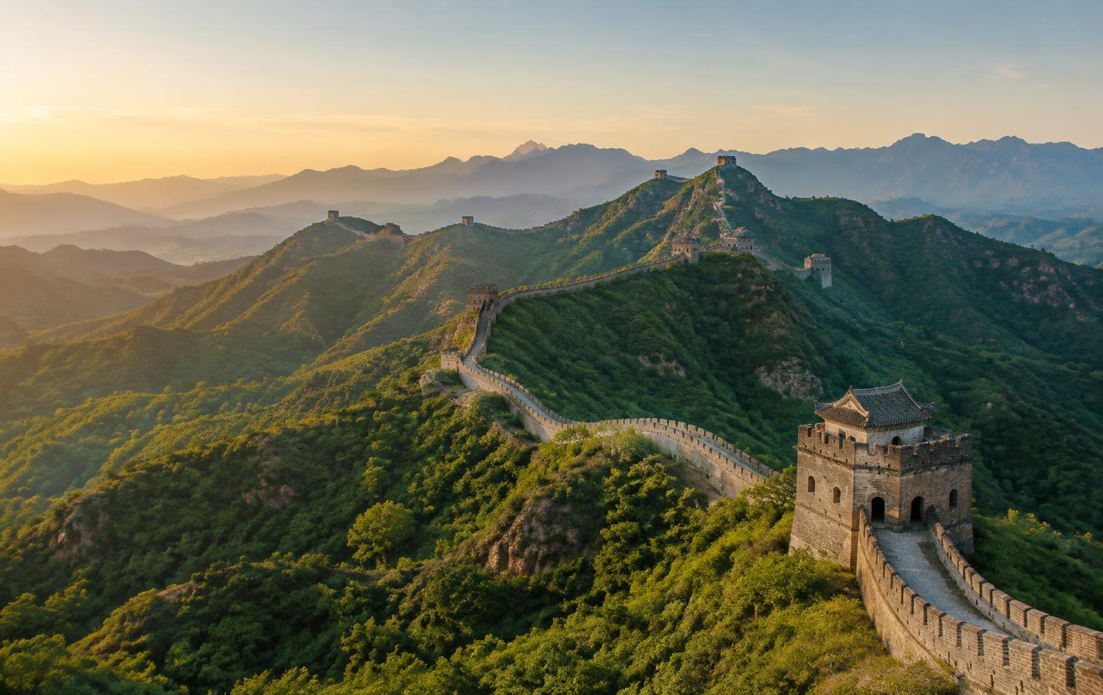 The Great Wall of China winding across green mountain ridges in warm morning light