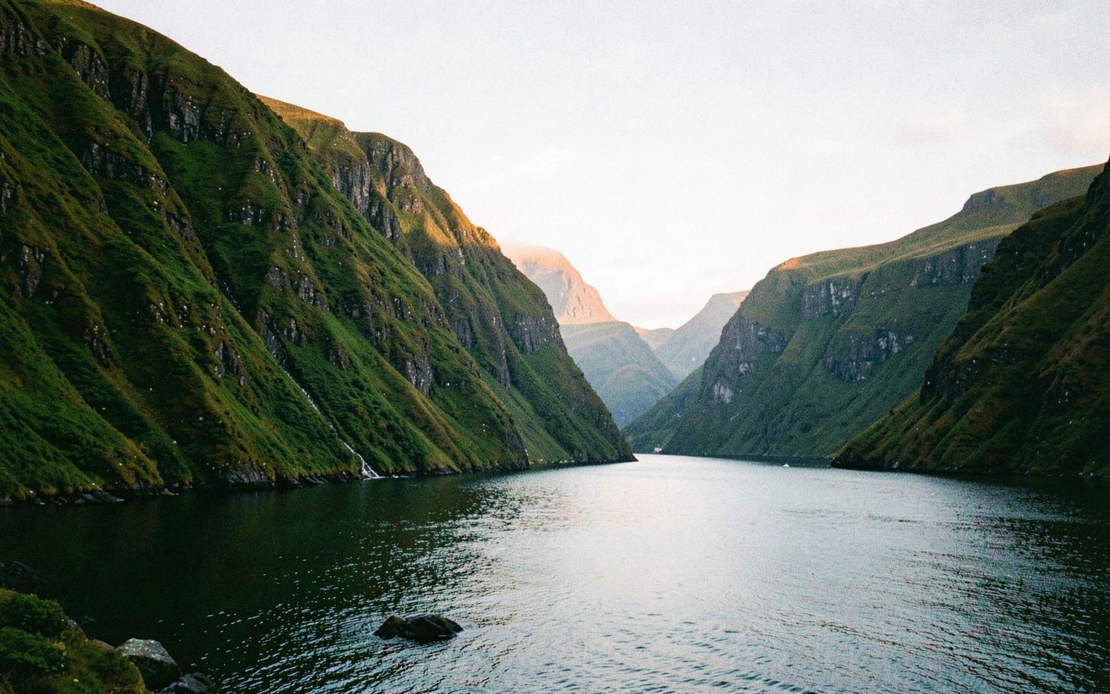A deep fjord at dawn with steep green cliffs falling into still water
